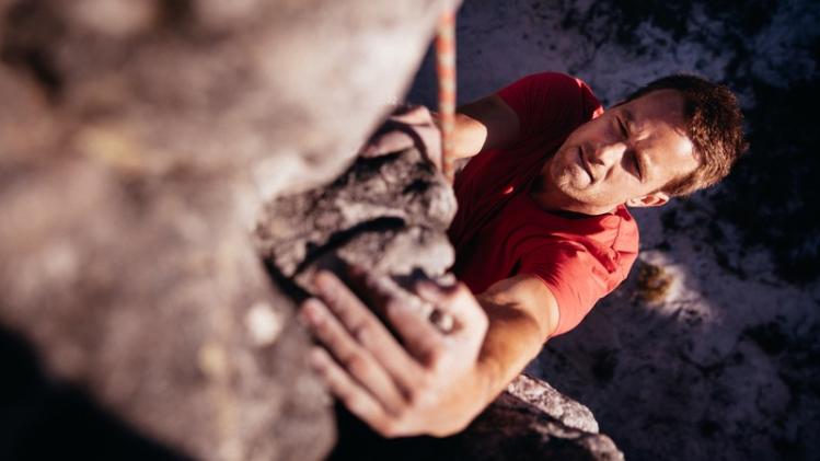Focussed Rock climber holding on grip while hanging from boulder