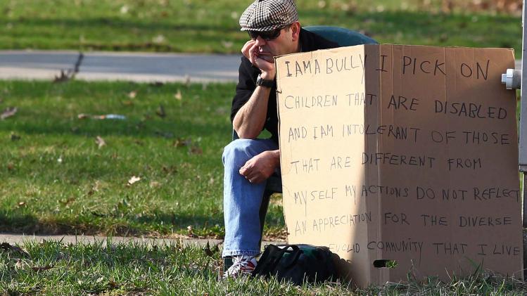 Aviv sits with an "I am a bully" sign at a street corner in the Cleveland suburb of South Euclid