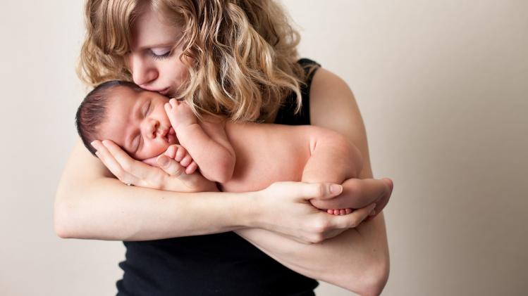 Loving Mother Holding and Kissing Newborn Baby