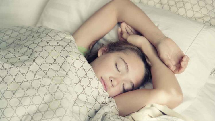 Young girl peacefully sleeping in light bedsheets.