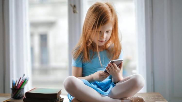 calm-small-ginger-girl-sitting-on-table-and-using-smartphone-3755620