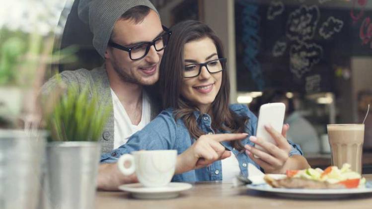 Embracing couple using mobile phone in cafe