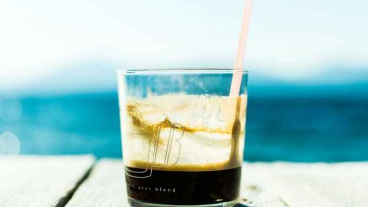 Glas met koffie, water op de achtergrond
